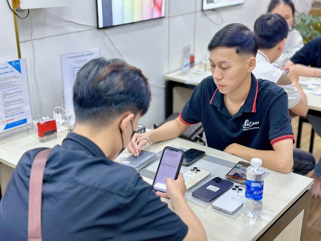 Khách hàng đang kiểm tra iPhone cũ đổi trả tại cửa hàng Táo 247 Đà Nẵng cùng nhân viên tư vấn